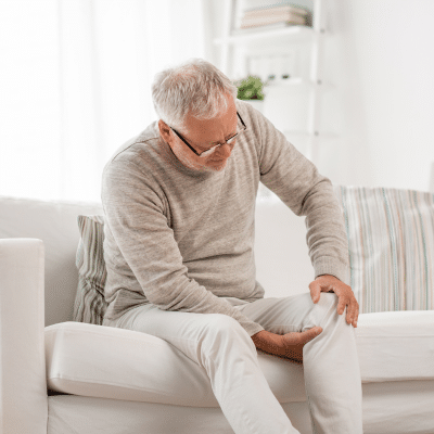 Older man sitting on a couch and holding his right knee with both hands because of pain