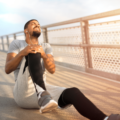 5 common sports injuries and prevention tips for staying active 4 Man holding knee in pain while sitting on a boardwalk, representing common sports injuries